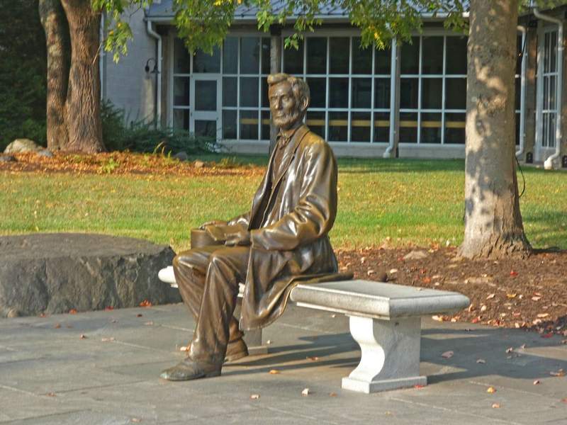 A bronze stature of Abraham Lincoln seated on a white stone bench.