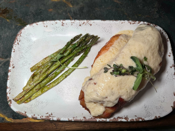 Chicken with cheese and green asparagus on a white plate. 